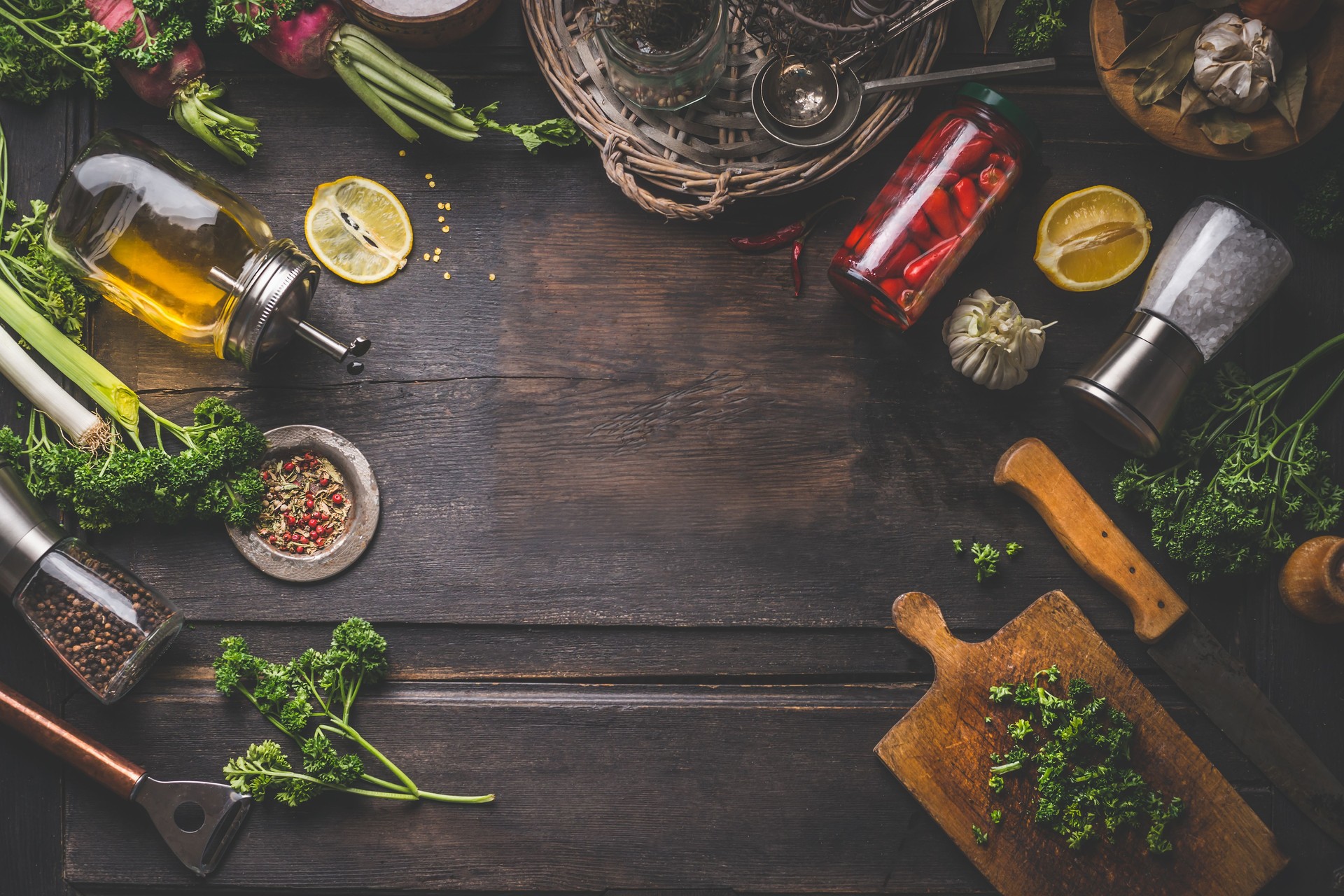 Dark food background with various ingredients and jars with preserved vegetables, seasoning and kitchen tools for tasty home cooking.